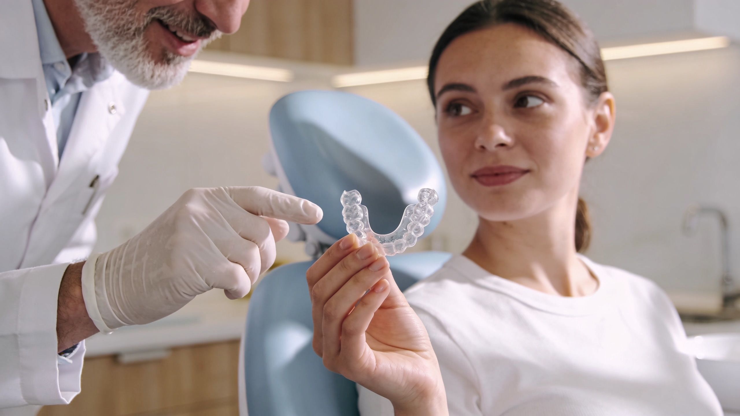 A dentist shows a clear dental aligner tray to a female patient during a consultation at a clinic.