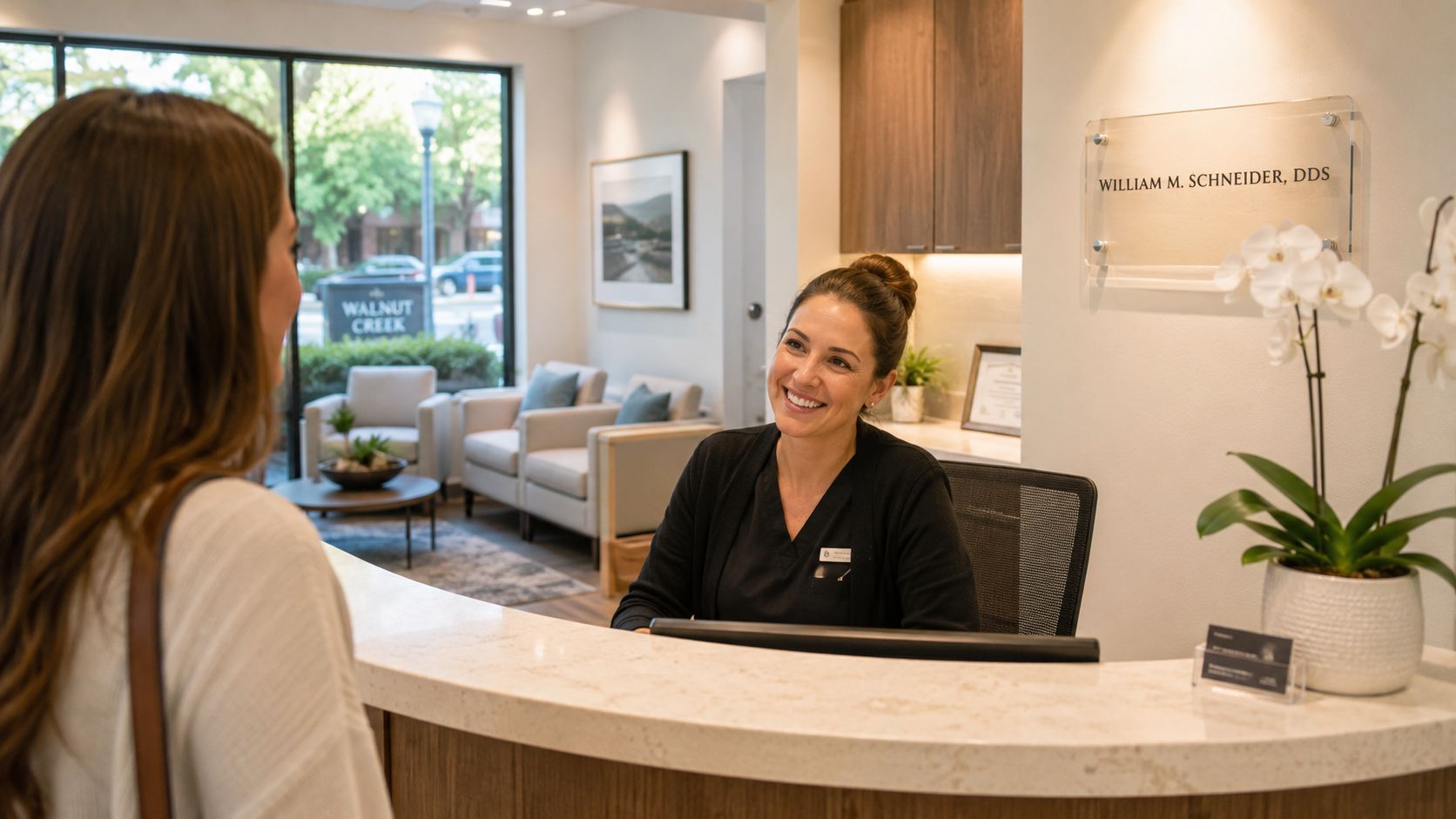 A friendly dental receptionist smiling at a patient at the front desk of a dental office.