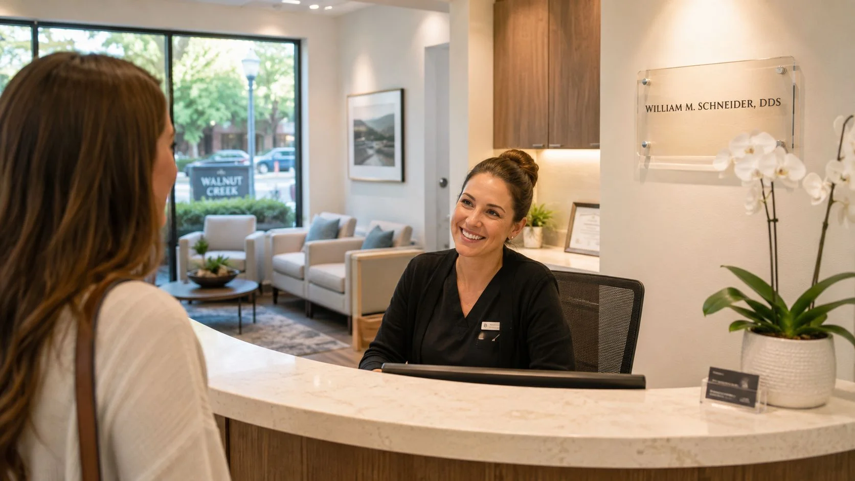 A friendly dental receptionist smiling at a patient at the front desk of a dental office.